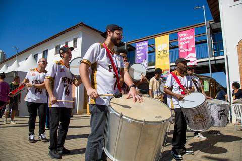 Ritmista de óculos escuros tocando surdo de marcação com energia durante a apresentação da escola. Foto por Bruno Arita.'