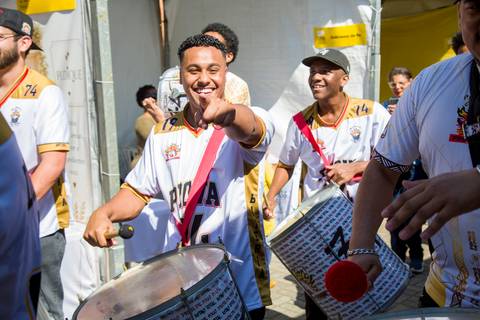close-up de ritmista da Prova de Fogo de Pirituba sorrindo e tocando repique de anel durante cortejo. Foto por Bruno Arita.'