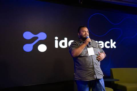 Palestrante com Microfone: Palestrante discursando no palco iluminado da IdealTrack sobre inovação e IA em São Paulo. Foto por Bruno Arita.'
