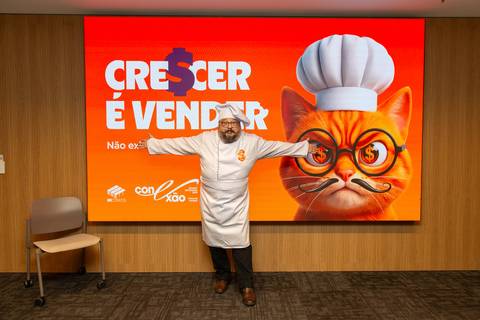 Abertura Temática Fome de Vendas: Palestrante de dólmã no palco à frente do painel digital com mascote do Summit BRCondos. Foto por Bruno Arita.'