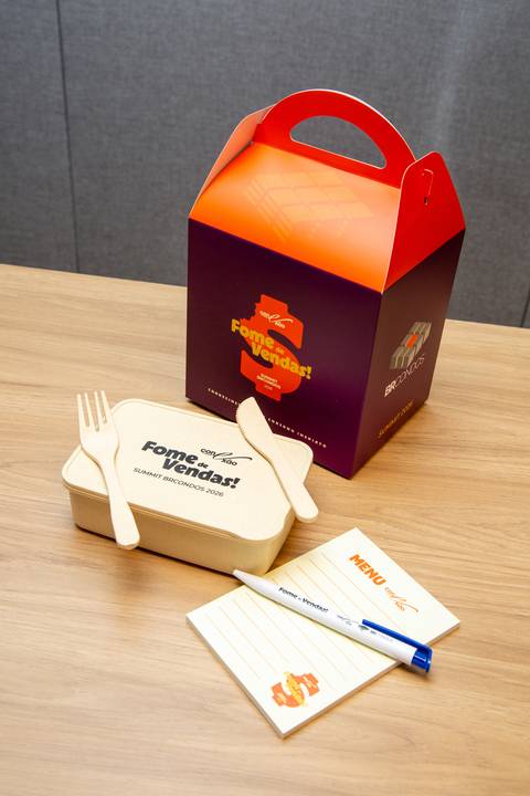 Kit do Participante e Mimos: Caixa surpresa, bloco de notas, caneta e talheres ecológicos sobre a mesa do evento. Foto por Bruno Arita.'