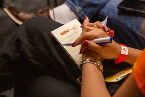 Anotações durante Palestra: Participante fazendo anotações no bloco de notas personalizado no colo durante o evento. Foto por Bruno Arita.'