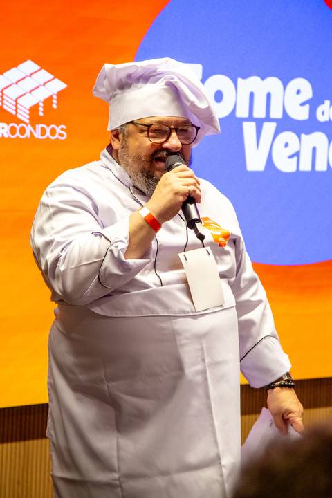 Palestrante Principal de Dólmã: Executivo da BRCondos discursando com microfone caracterizado como chef no palco. Foto por Bruno Arita.'