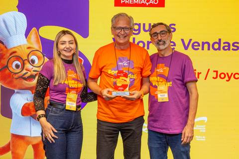 Três participantes do evento Summit BRCondos reunidos no palco durante a cerimônia de premiação, segurando um troféu em formato do selo Fome de Vendas. Foto: Bruno Arita.'