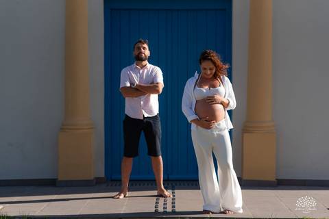 Casal em pé lado a lado, em frente à porta azul, em clima leve e descontraído'