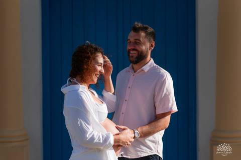 Casal de mãos dadas, trocando sorrisos em frente ao cenário urbano'