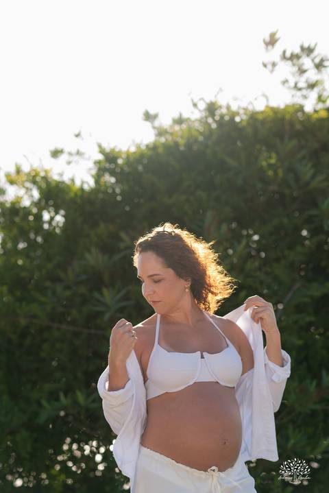 Retrato da gestante com luz natural entre árvores, em momento de introspecção'