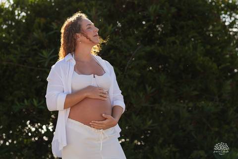 Gestante acariciando a barriga, cercada pela natureza, em clima de paz'