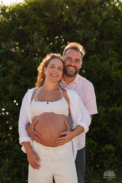 Retrato do casal sorrindo, com foco na barriga da gestação'