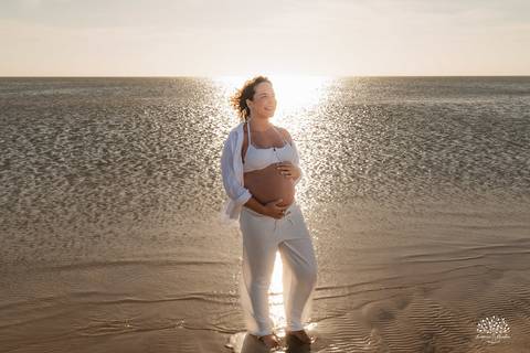 Gestante na beira do mar, com reflexo da luz do sol na água'
