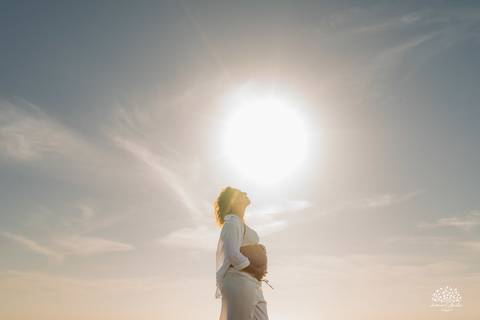 Gestante na beira do mar, com reflexo da luz do sol na água'