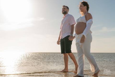 Casal caminhando na praia ao entardecer, com luz dourada'