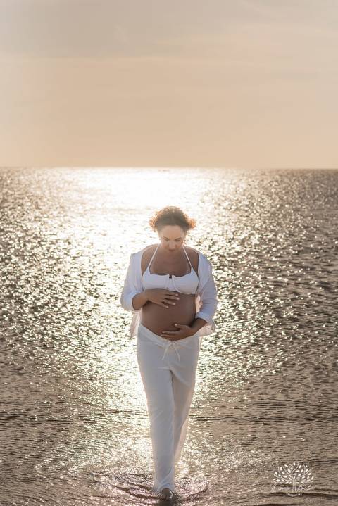 Gestante olhando para a barriga, refletida pela luz do mar'