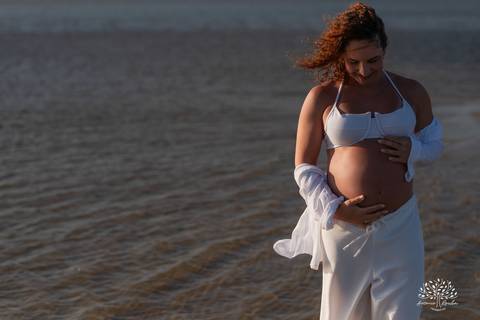 Gestante sozinha na beira da água, sentindo o vento no rosto'