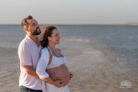 Casal posando juntos na praia, com horizonte ao fundo'