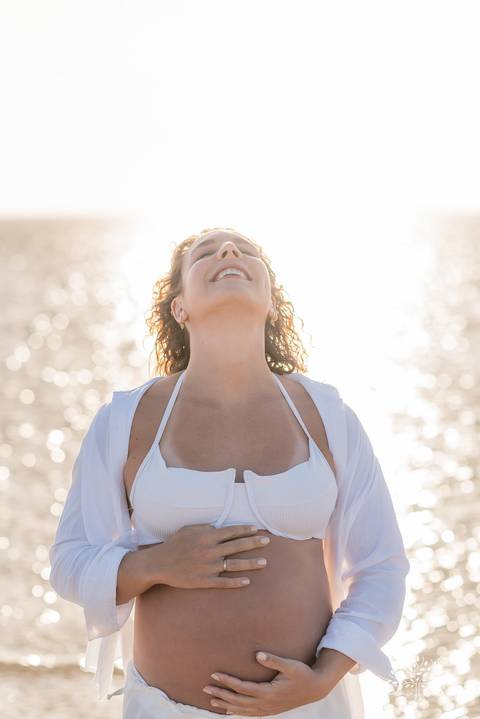 Retrato da gestante sorrindo para o céu, com luz refletida no mar'