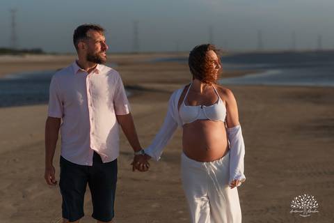 Casal caminhando de mãos dadas na praia, ao final do dia'