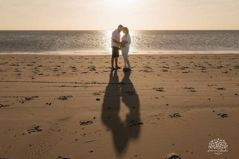 Silhueta do casal ao pôr do sol, refletida na areia molhada'