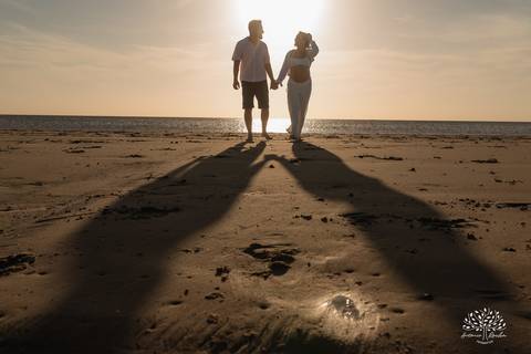 Casal caminhando em direção ao horizonte, deixando marcas na areia.'