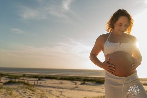 Gestante acariciando a barriga contra o pôr do sol.'