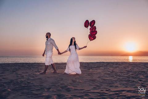 noivos caminhando na areia com por do sol ao fundo e carregando balões bexigas de coração em ensaio pré-wedding na praia fotografado por Say Cheese Fotografia'