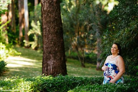 gestante de vestido florido em caminho de folhagens'