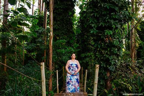 gestante em ponte de madeira em meio a grandes aárvores'