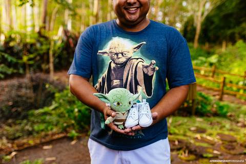 pai sorridente segurando boneco do Mestre Yoda e sapatinho de bebe em ensaio de gestante'