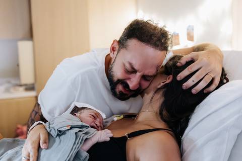 foto de pai e mãe se abraçando com bebê recém nascido em seu colo'