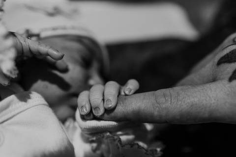 bebê recém nascido segurando dedo em preto e branco'