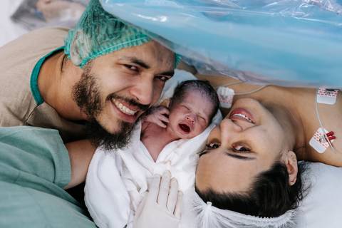 Foto do casal sorrindo com o bebê após o nascimento'