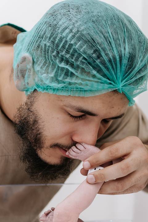 Foto do pai beijando o pé do recém-nascido no centro cirúrgico'