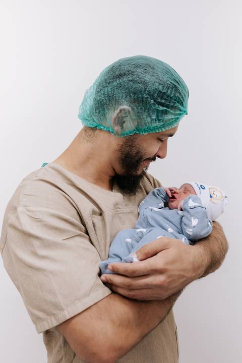 Foto do pai segurando o recém-nascido no colo com cuidado'