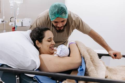 Foto do pai apoiando a mãe com o recém-nascido no colo'