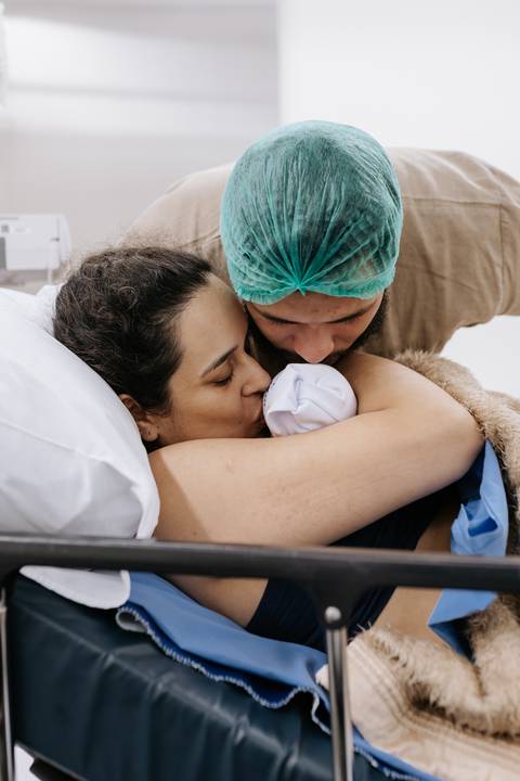 Foto aproximada do casal abraçado com o bebê após o parto'