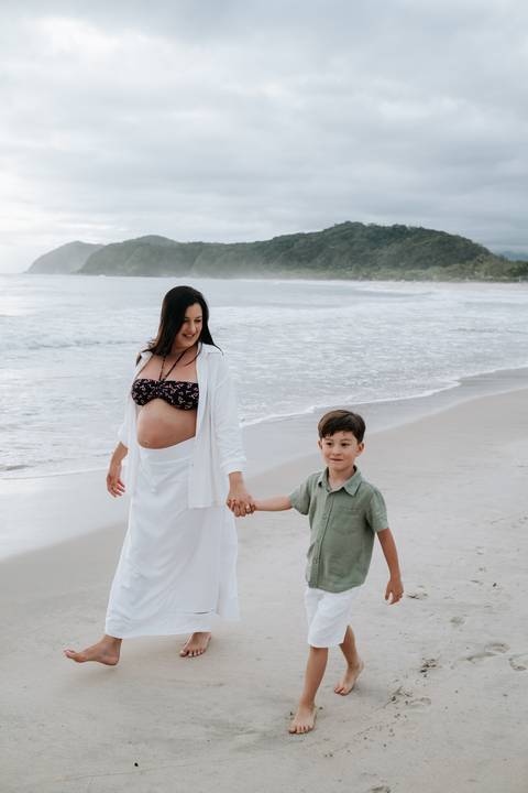 Foto da gestante caminhando na areia da praia com o filho'