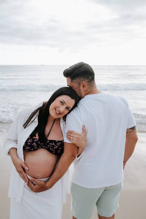 Foto do casal abraçado na praia durante ensaio gestante externo'