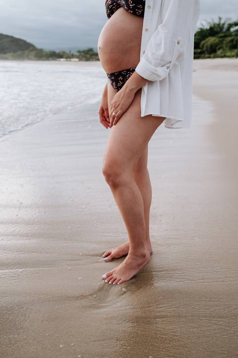 Foto do detalhe da barriga da gestante na areia da praia'