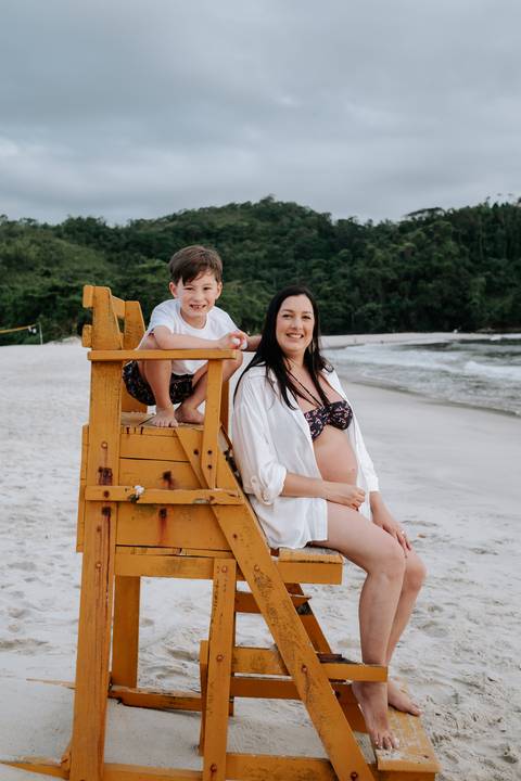 Foto da gestante e filho sentados em cadeira de salva-vidas na praia'