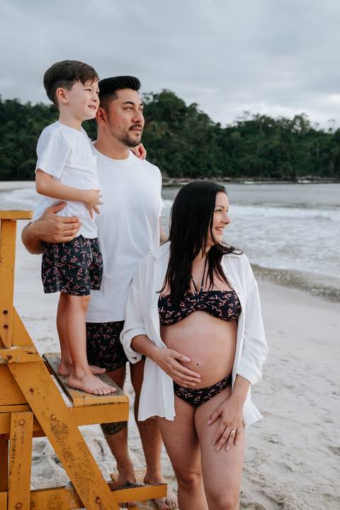 Foto da família sorrindo na areia com o mar ao fundo'