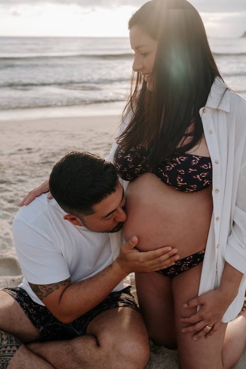 Foto do pai beijando a barriga da gestante na beira do mar'