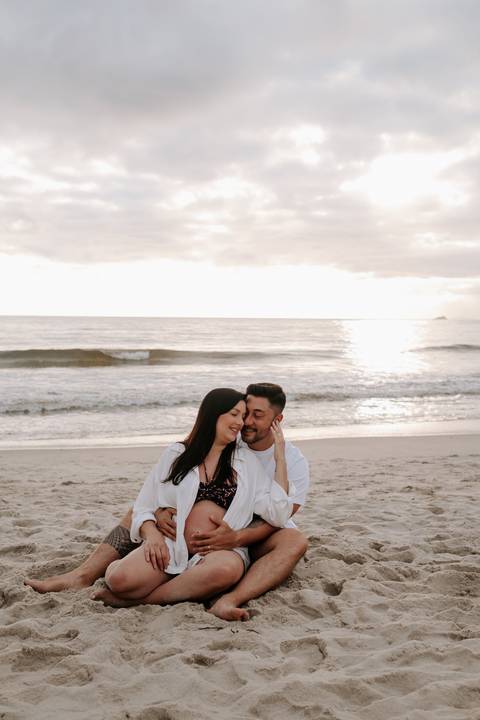 Foto do casal sentado na areia da praia em momento de conexão'