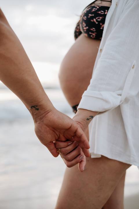 Foto do detalhe das mãos do casal  na praia'