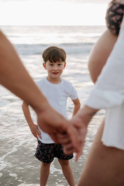 Foto do filho sorrindo entre os braços dos pais na praia'