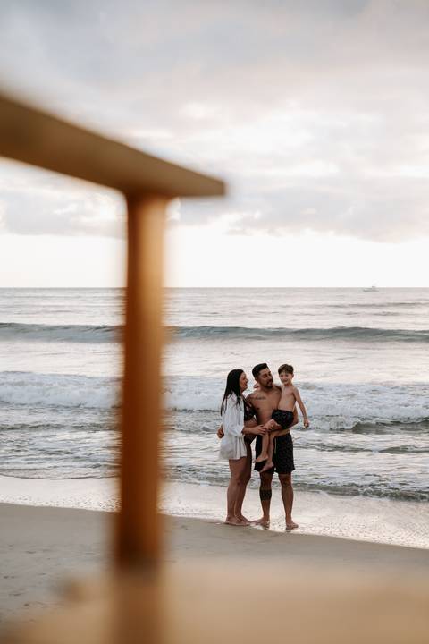 Foto do casal com o filho no colo na beira do mar'