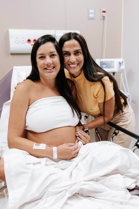 Foto da gestante sorrindo com acompanhante durante o pré-parto no hospital.'