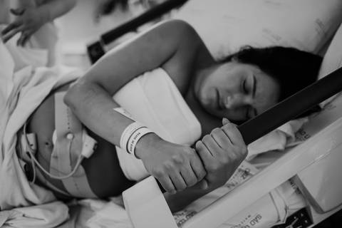 Foto em preto e branco da gestante segurando as barras de apoio no parto.'