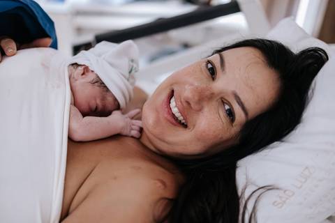 Foto da mãe sorrindo com o recém-nascido após o nascimento.'