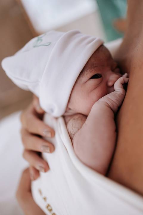 Foto aproximada do rosto do recém-nascido no colo da mãe.'