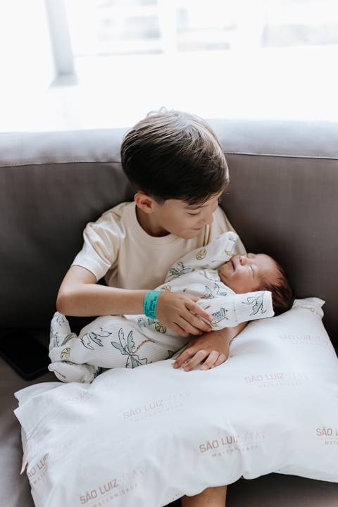 Foto do irmão mais velho segurando o recém-nascido no colo.'